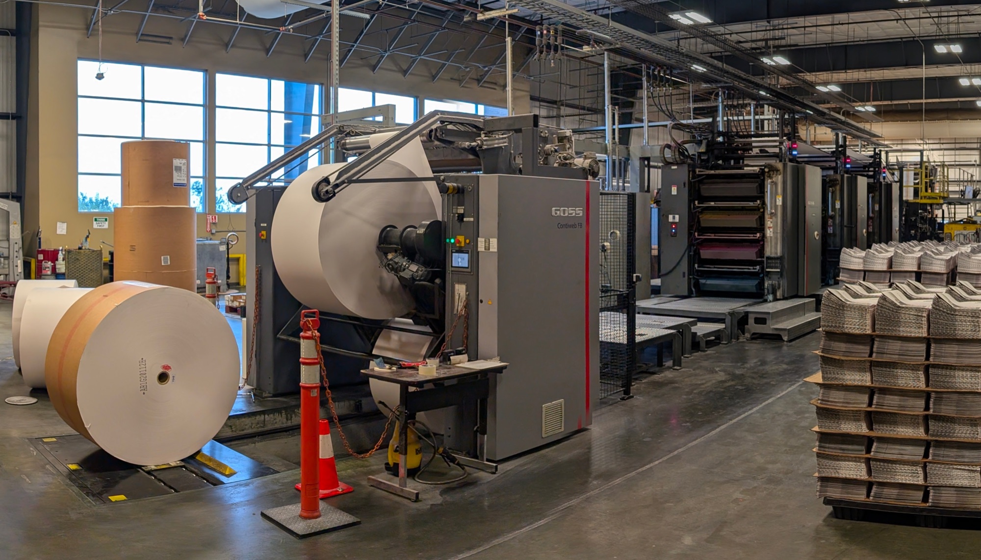 Community Impact Printing production floor in Pflugerville, Texas — GOSS press with paper rolls and pallets of printed product